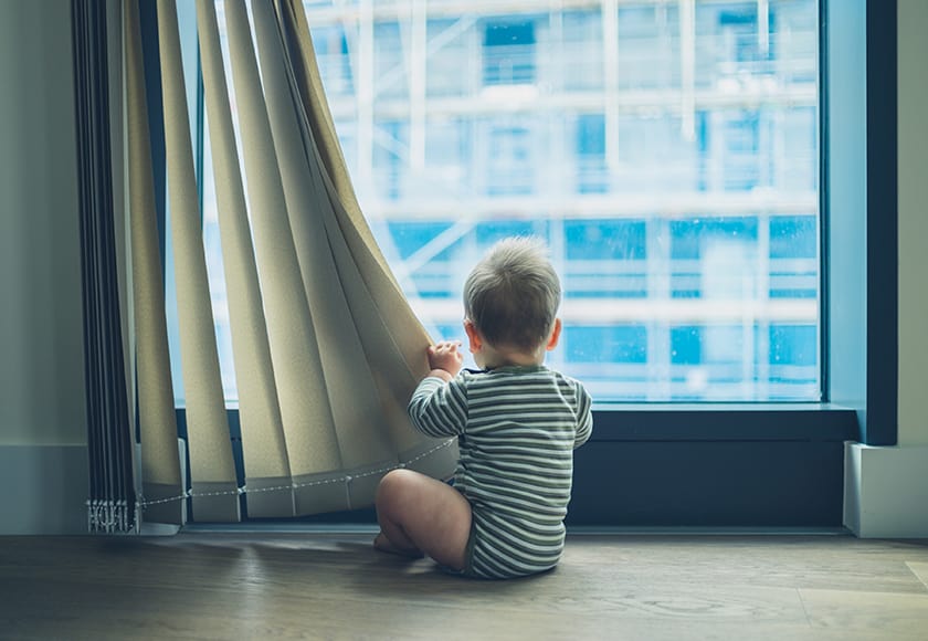 child sitting in front of corded blinds