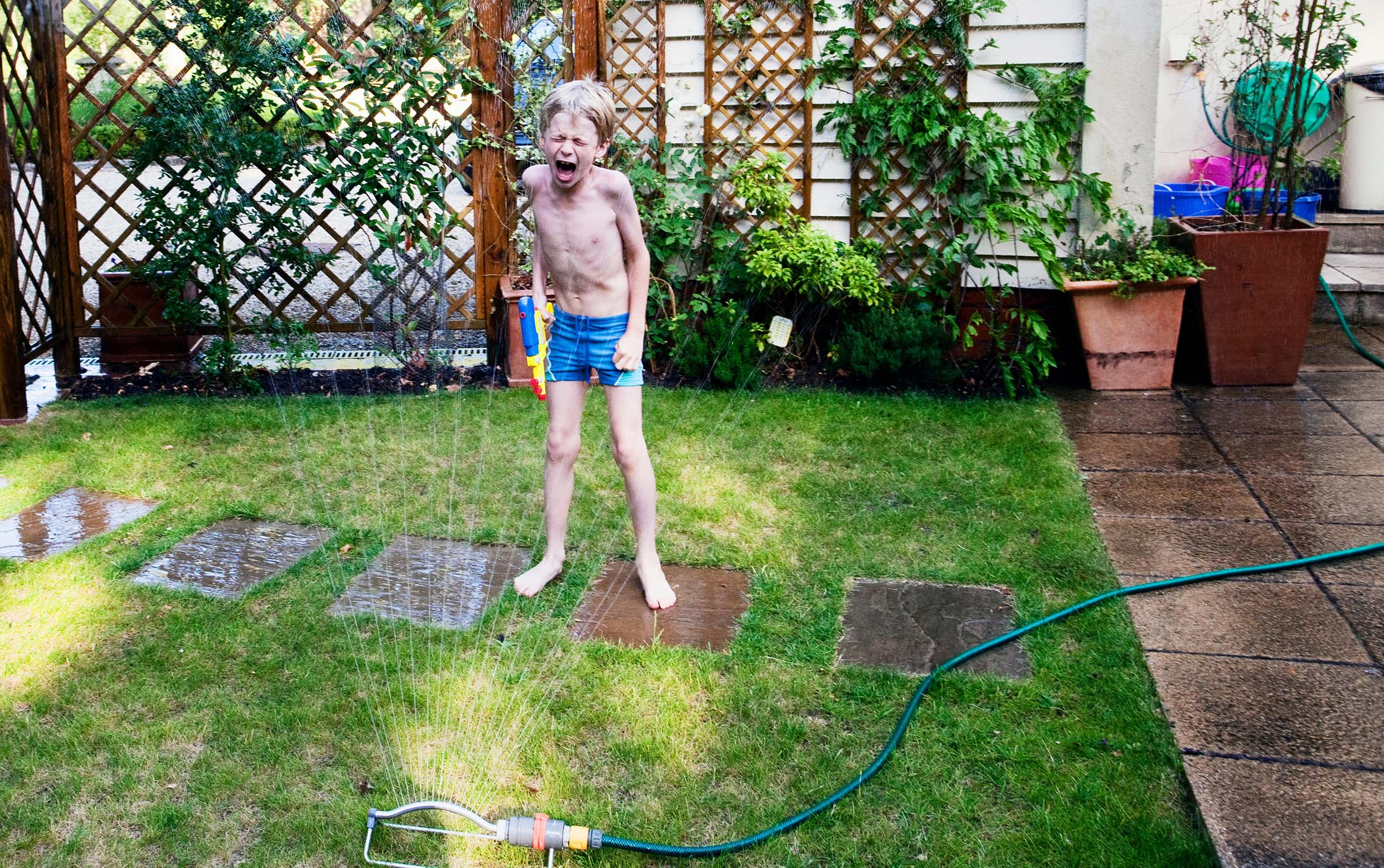 boy playing in sprinkler in backyard